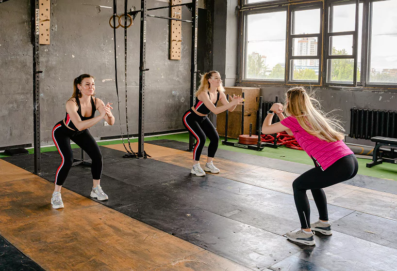 Three women performing squats in a CrossFit gym, focusing on strength training and fitness.
