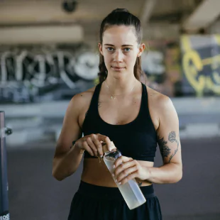 A woman in a sports bra and shorts holds a water bottle, ready for a workout or exercise session.