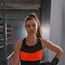 A woman wearing a black and orange sports bra and shorts stands confidently, showcasing her athletic attire.